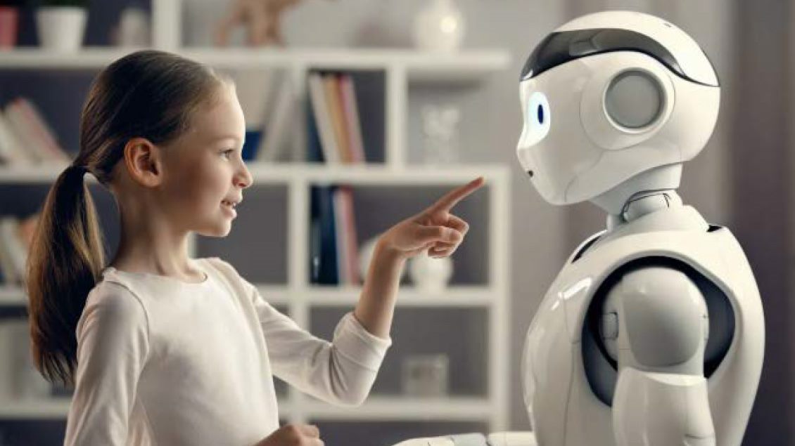 Devojčica drži tablet i razgovara sa humanoidnim robotom u moderno opremljenoj sobi.