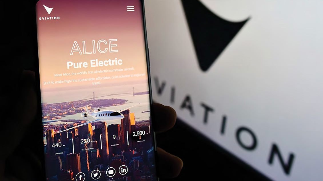 Na pametnom telefonu je prikazana promotivna stranica za „Alice“, prvi električni putnički avion, a u pozadini se vidi zamagljeni logo kompanije.