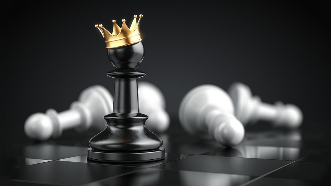 Crni šahovski pion sa zlatnom krunom među oborenim figurama – simbol uspeha i liderstva.