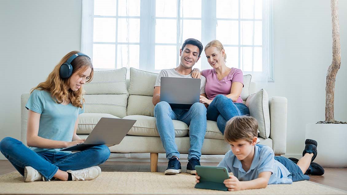 Porodica u dnevnoj sobi koristi Wi-Fi – roditelji na laptopu, tinejdžerka sa slušalicama i laptopom, dete sa tabletom.