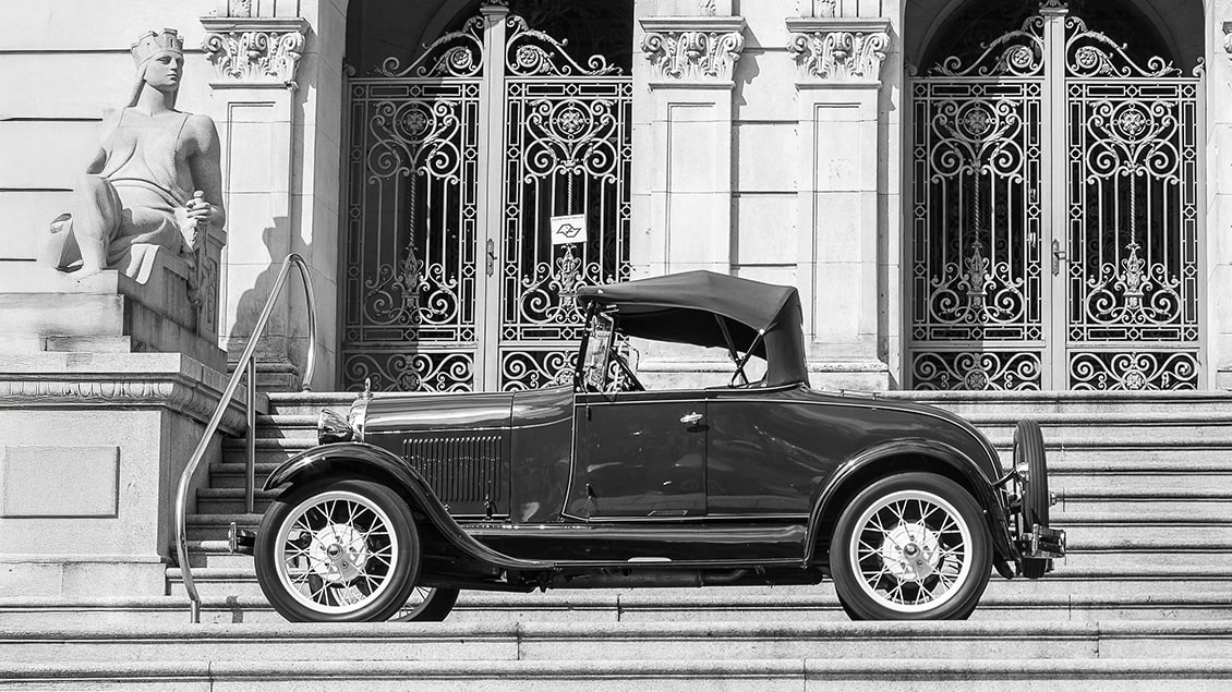 stari automobil model T ispred zgrade sa stepenicama i skulpturom u crno-beloj fotografiji