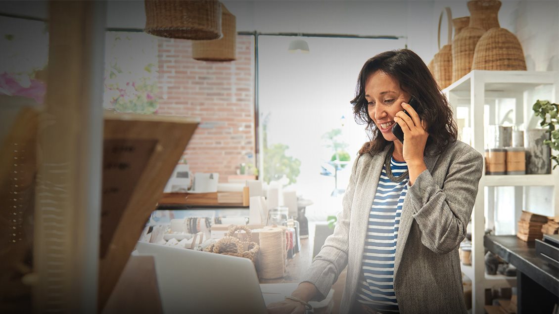 Preduzetnica u maloj prodavnici koristi laptop i razgovara telefonom.