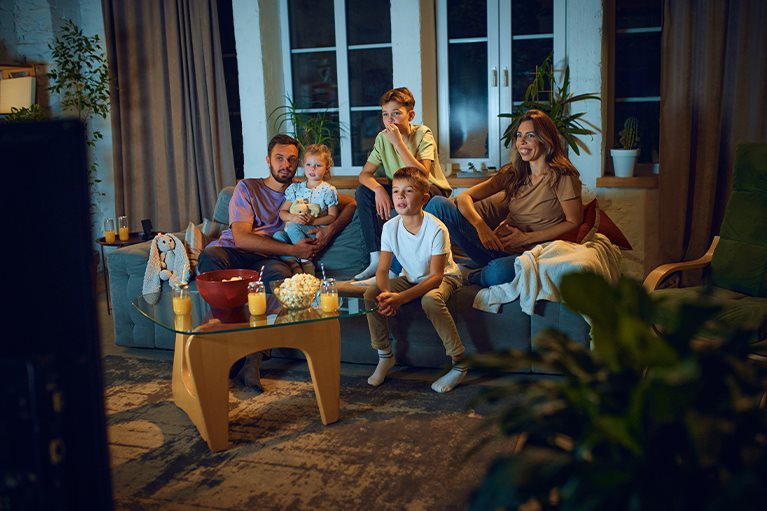 Porodica zajedno gleda televiziju u dnevnoj sobi tokom večernjeg programa.
