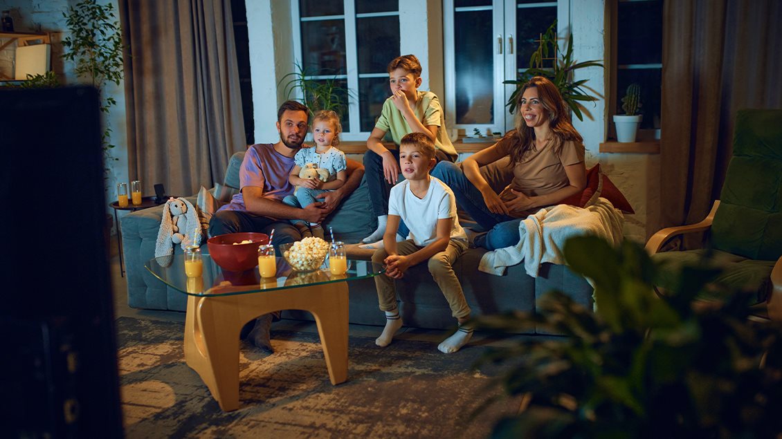 Porodica zajedno gleda televiziju u dnevnoj sobi tokom večernjeg programa.