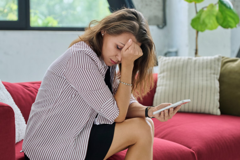 Digitalni umor – žena sedi na kauču, umorna i zamišljena dok gleda u telefon.
