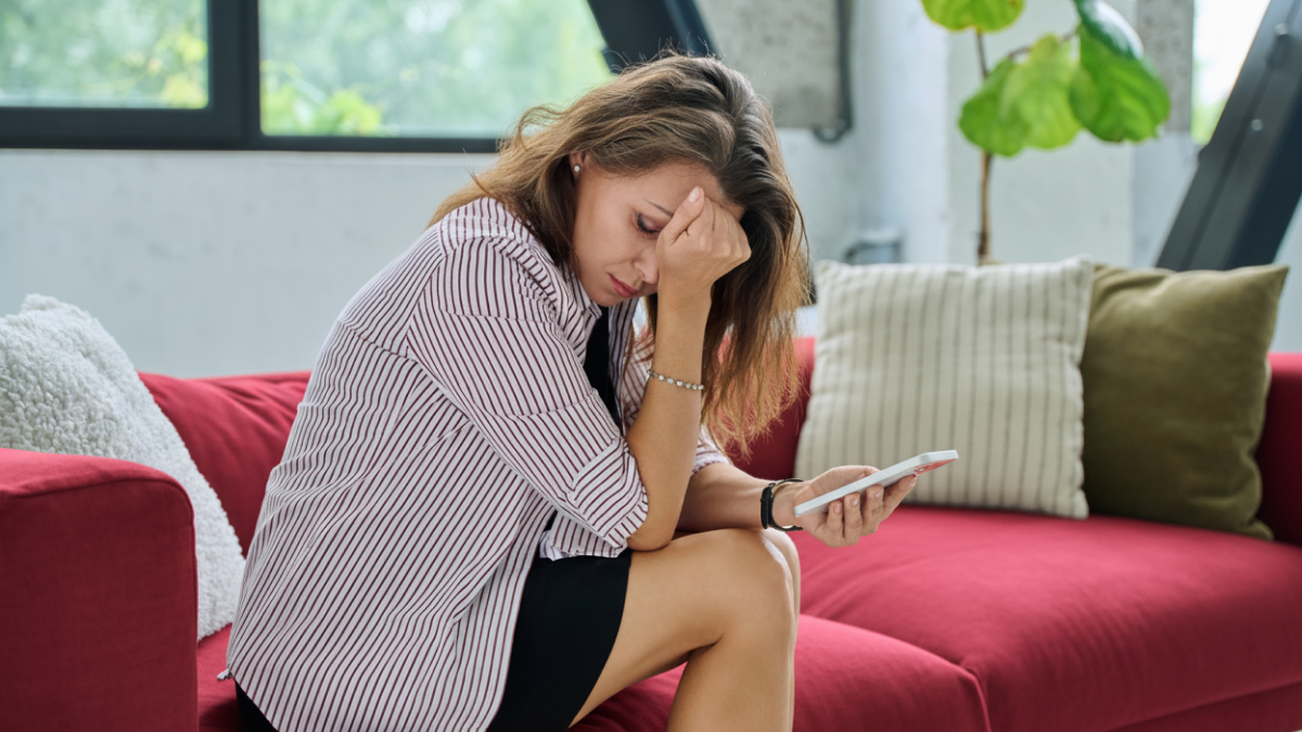 Digitalni umor – žena sedi na kauču, umorna i zamišljena dok gleda u telefon
