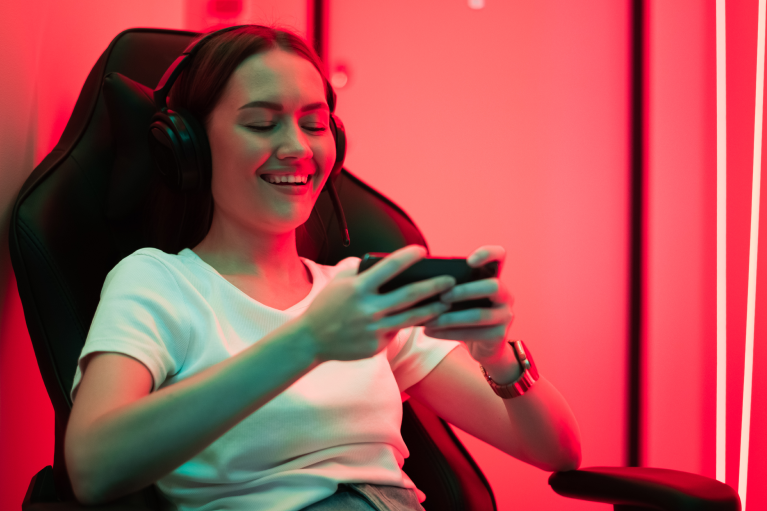 Devojka igra mobilne igre na telefonu sa slušalicama u gejming okruženju