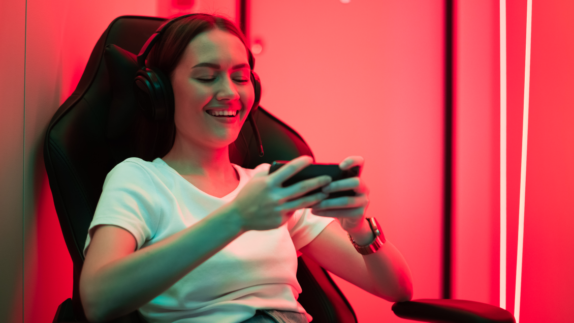 Devojka igra mobilne igre na telefonu sa slušalicama u gejming okruženju