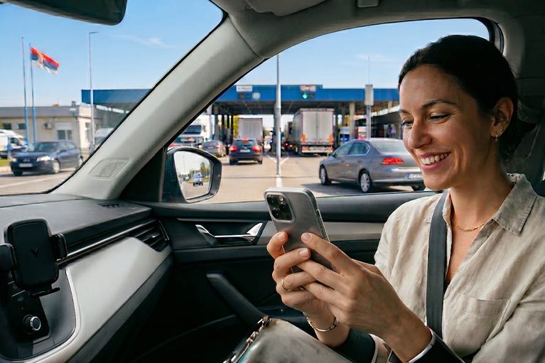 Žena u automobilu dobija SMS potvrdu o aktivaciji putnog osiguranja pri prelasku granice