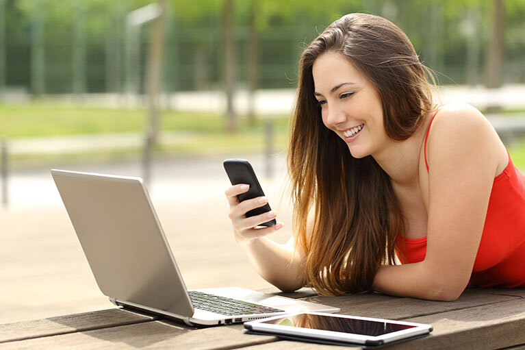 Devojka koristi mobilni telefon pored laptopa i tableta u parku