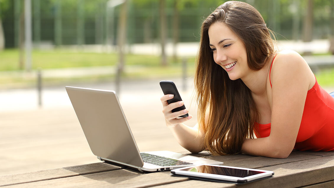Devojka koristi mobilni telefon pored laptopa i tableta u parku