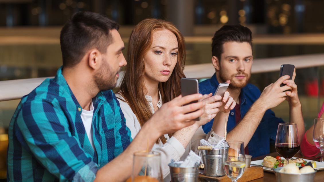 Ljudi za stolom koriste mobilne telefone tokom druženja