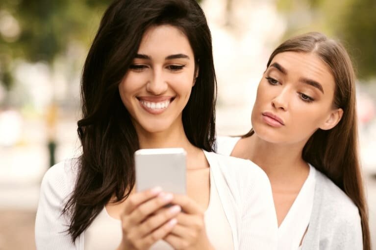 Žena koristi mobilni telefon dok druga osoba pokušava da vidi sadržaj poruka