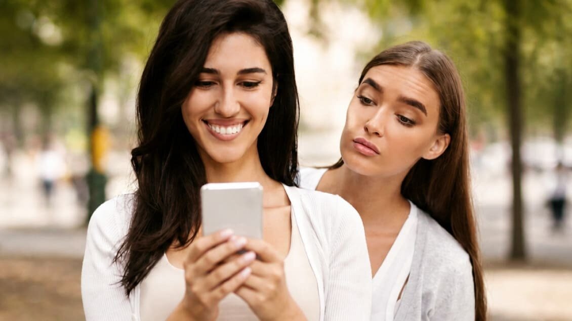 Žena koristi mobilni telefon dok druga osoba pokušava da vidi sadržaj poruka
